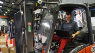 Technik provádí kontrolu použitého vysokozdvižného vozíku Technik s notebookem při kontrole vysokozdvižného vozíku k repasování